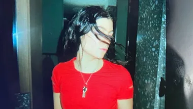 Singer Lorde posing for photo with eyes shut wearing red t-shirt.
