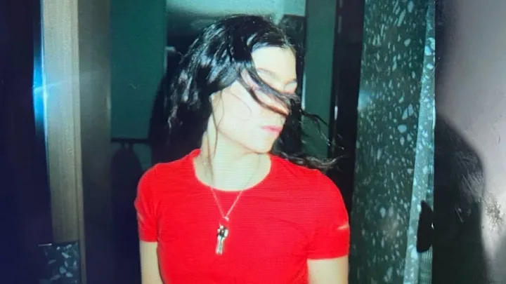 Singer Lorde posing for photo with eyes shut wearing red t-shirt.