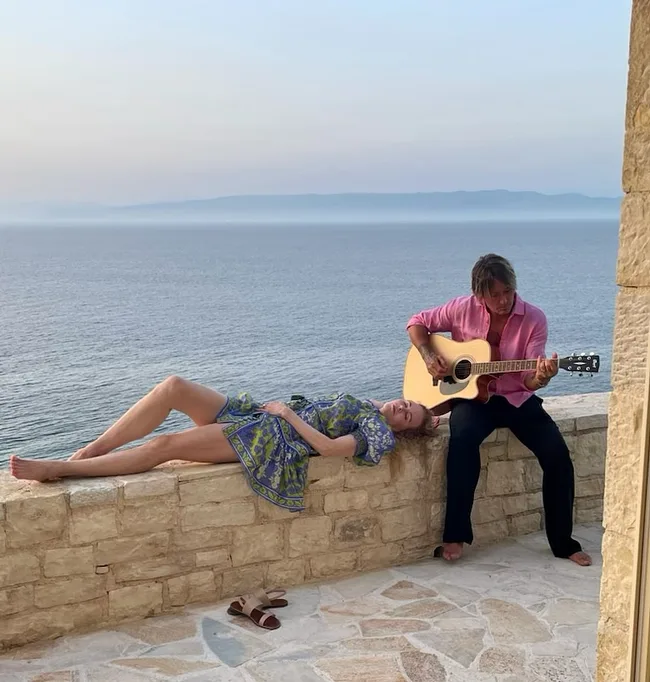 nicole kidman and keith urban on holiday. Keith plays the guitar while Nicole lays beside him on a stone wall.