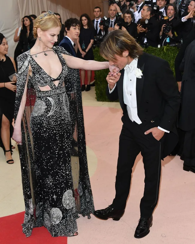 keith urban kisses nicole kidman's hand at the 2016 met gala while nicole kidman wears a black and silver dress adorned with moons