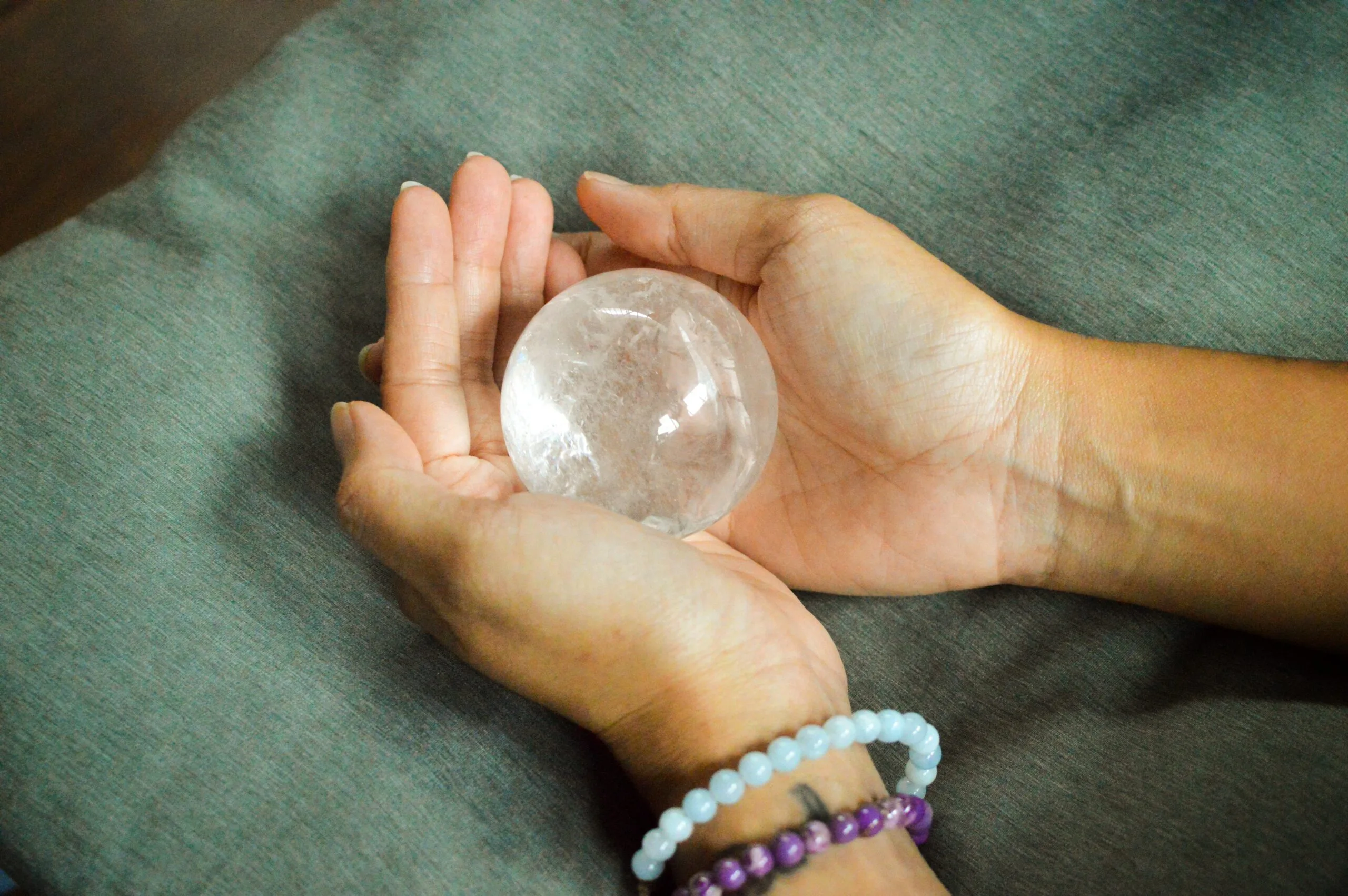 hands with crystal bracelets are holding clear quartz crystal sphere