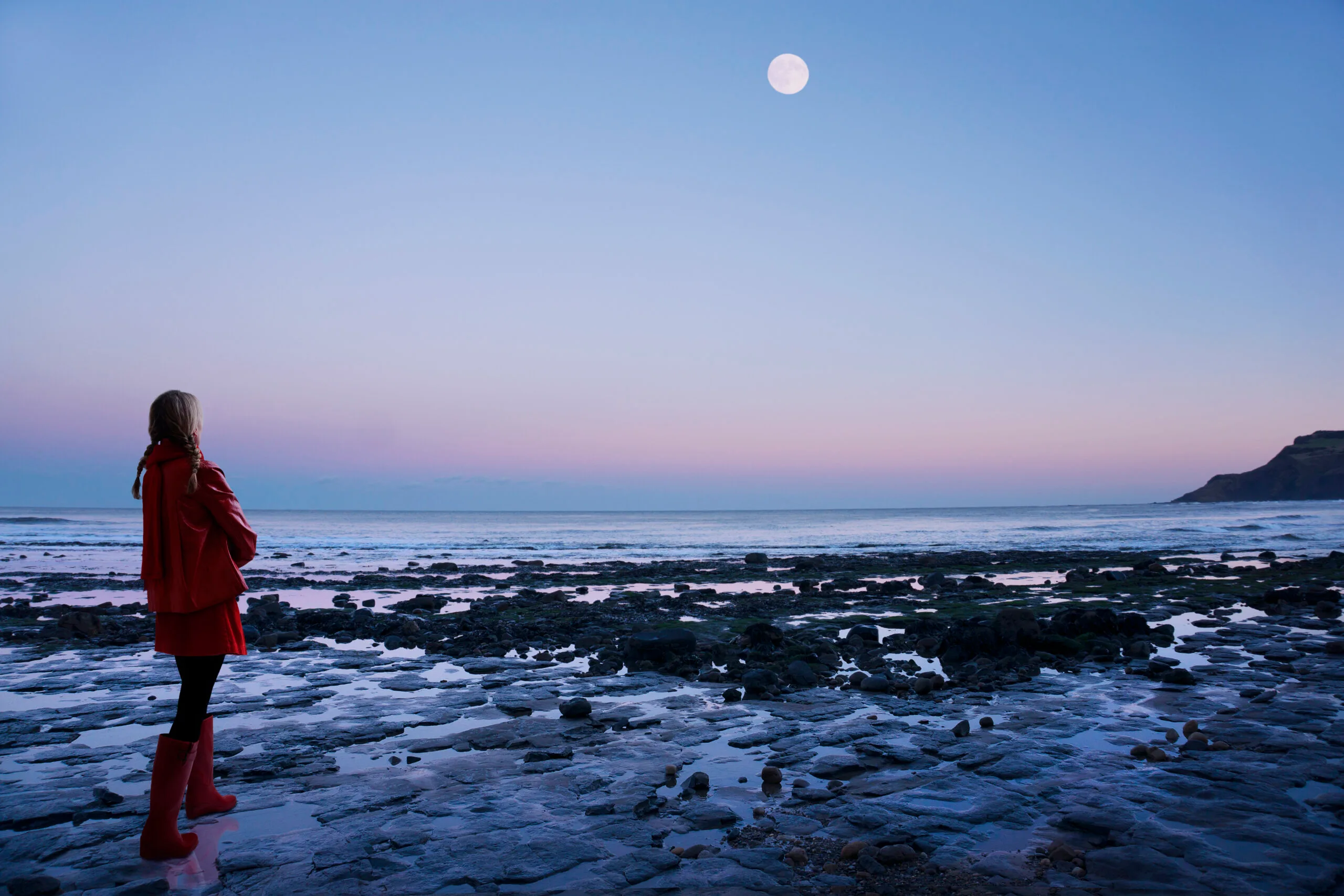 a woman walking along a beach during a full moon