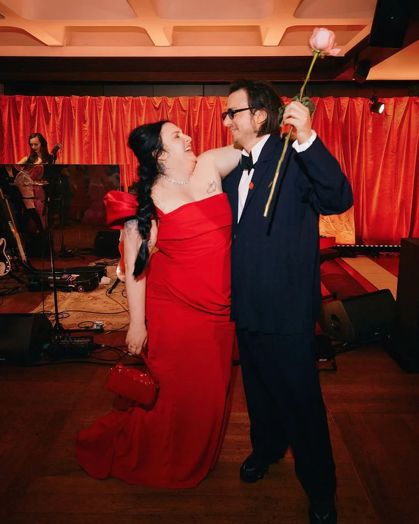 lena dunham and husband luis felber embrace behind the scenes of the too much premiere as Luis holds a long stemmed red rose