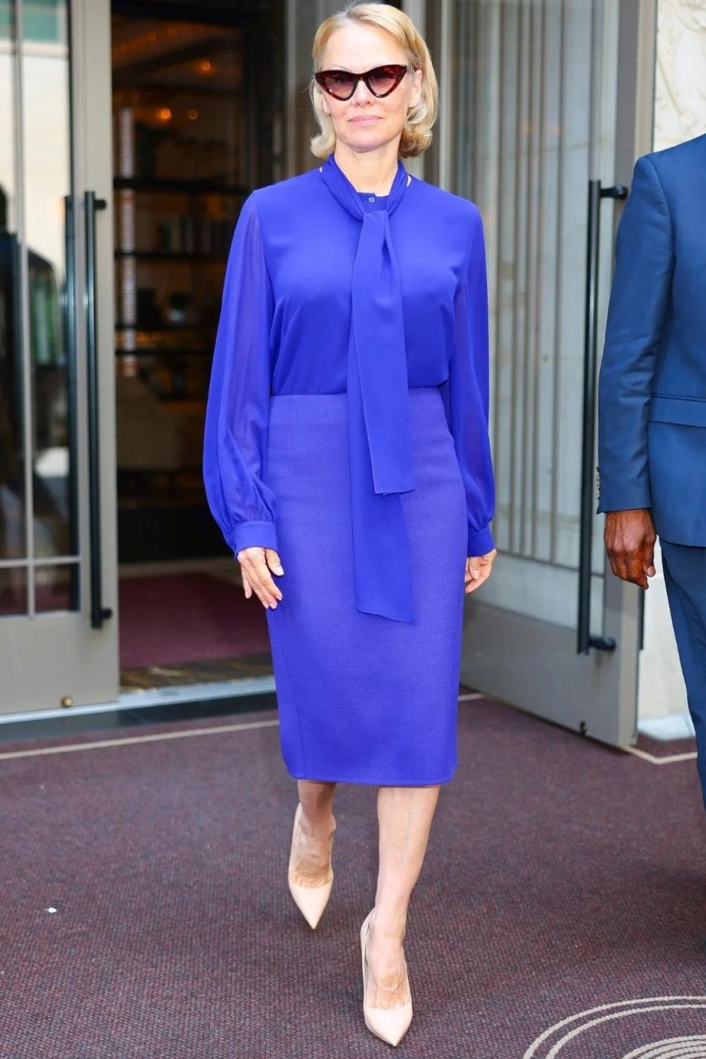 Pamela Anderson style wearing an electric blue long sleeve top and blue skirt.