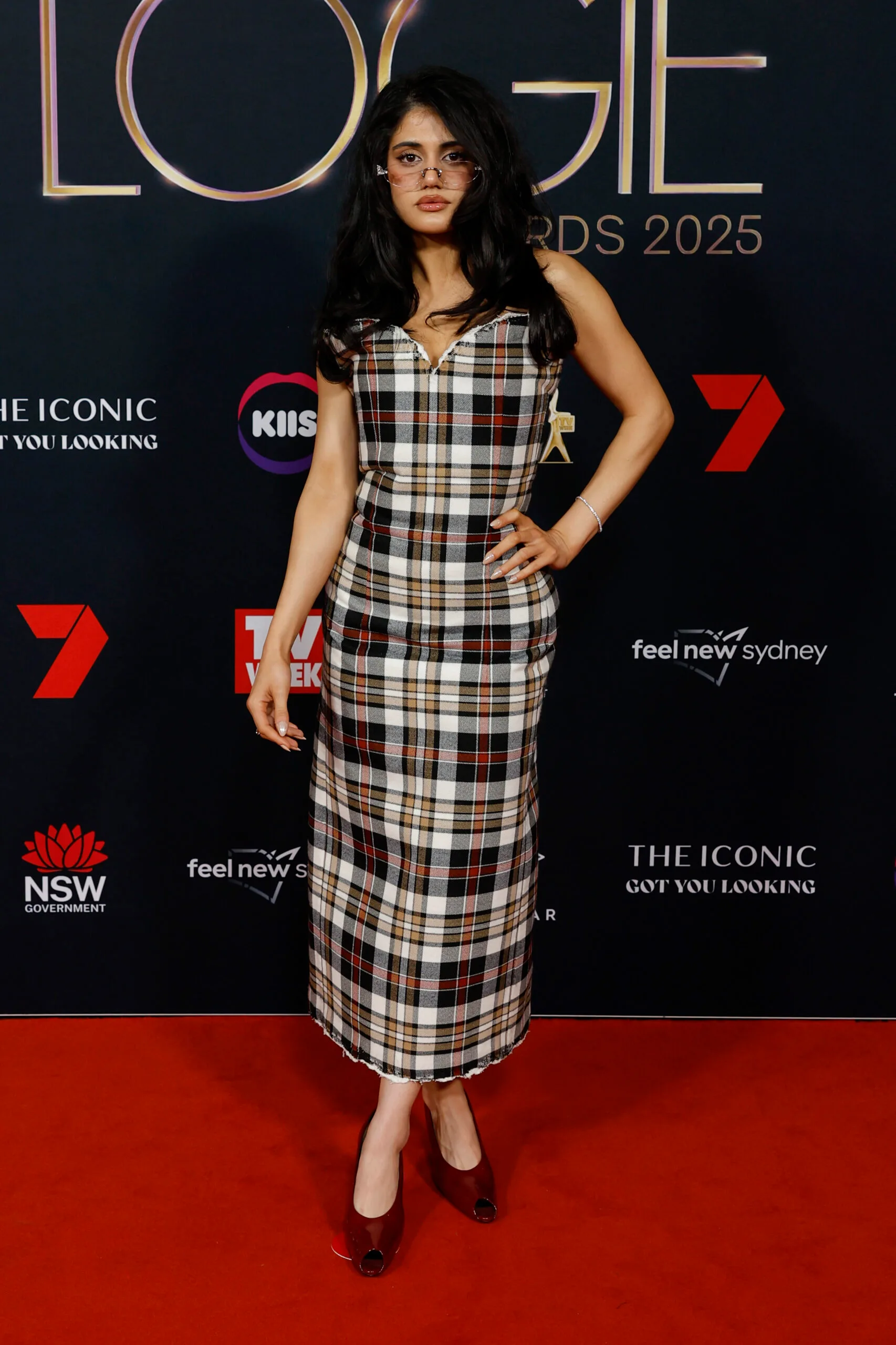 Woman with brown hair posing on a red carpet waring a checkered dress