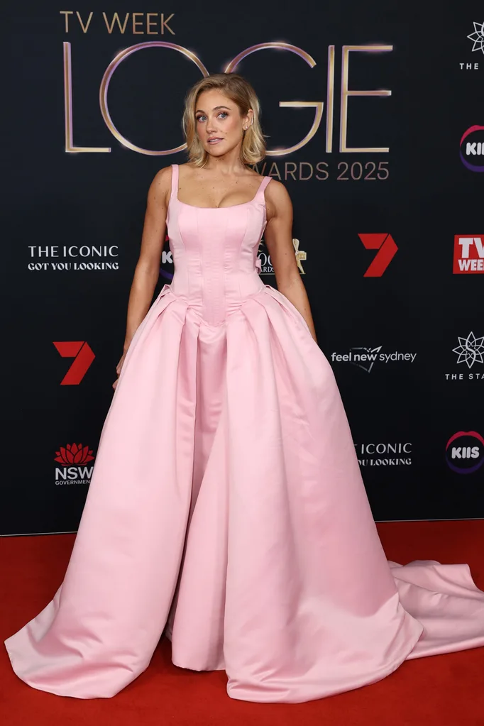 Woman with blonde hair posingin pink gown on a red carpet.