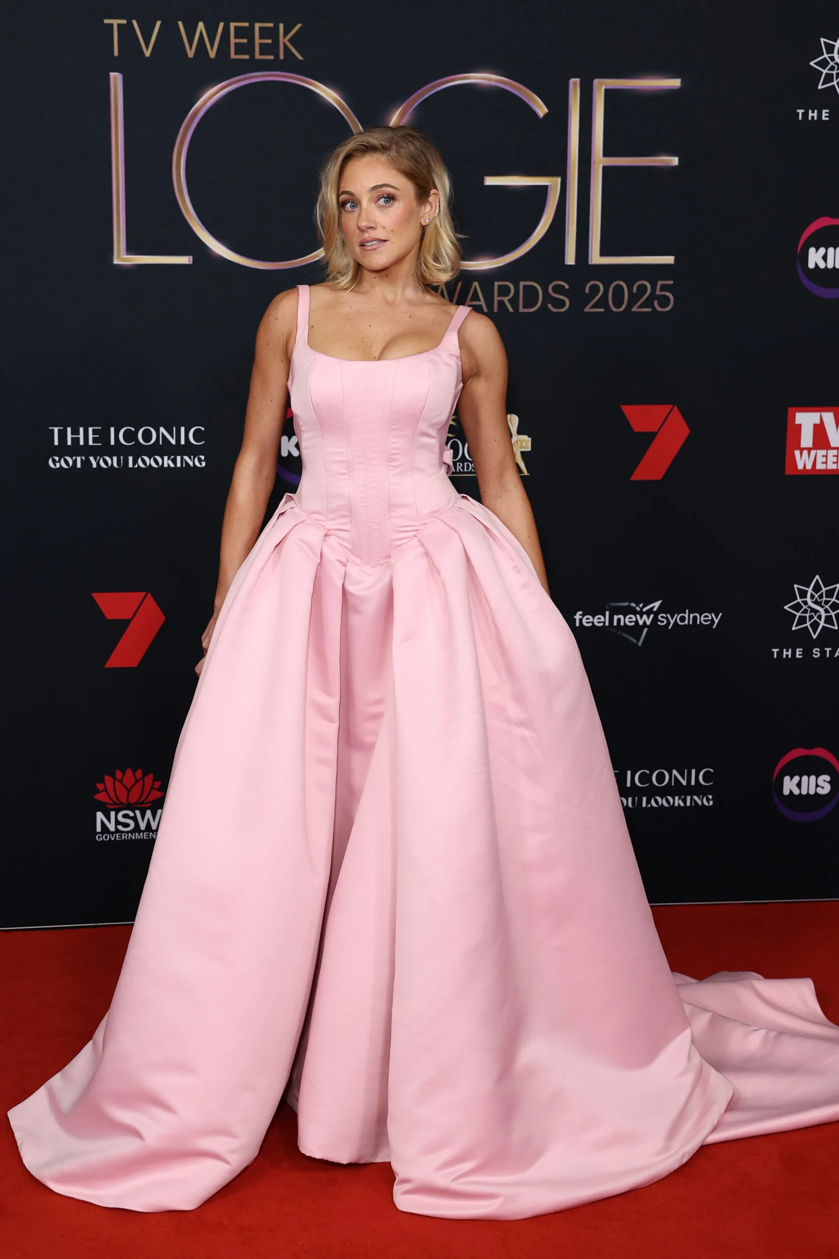 Woman with blonde hair posingin pink gown on a red carpet. 