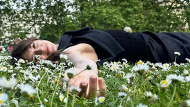 Actor, Daisy Edgar-Edgar Jones lays on her back in a field of flowers.