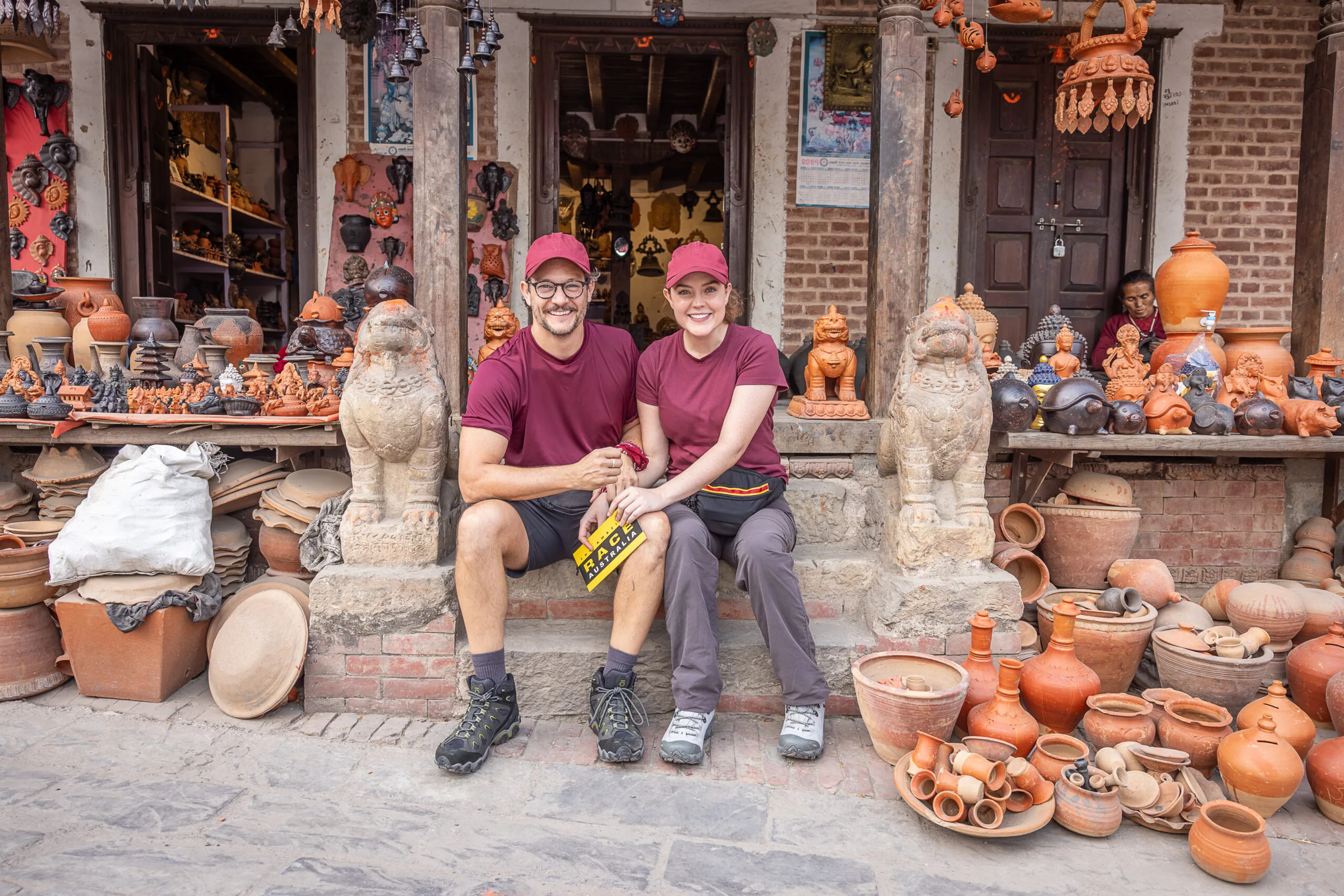 rob mills and georgie tunny smiling on a stair stoop surrounded by statues for the amazing race