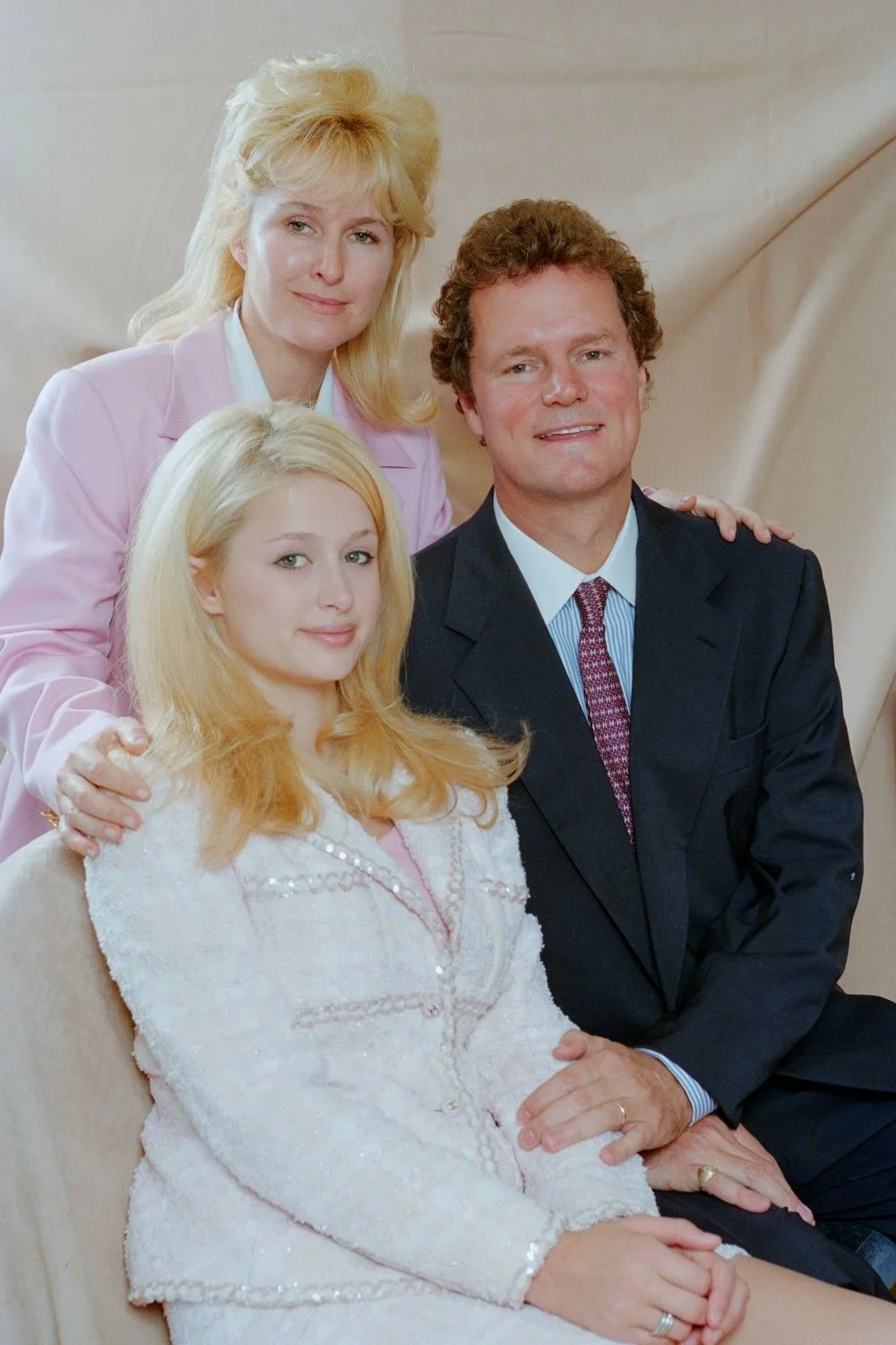 Young Paris Hilton with bright blonde hair alongside her parents for a family portrait.