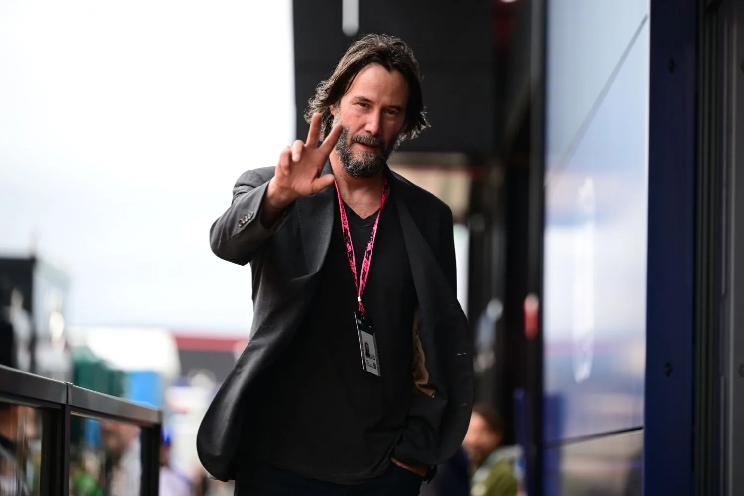keanu reeves, a tall man with long dark hairand facial hair, waving at the camera