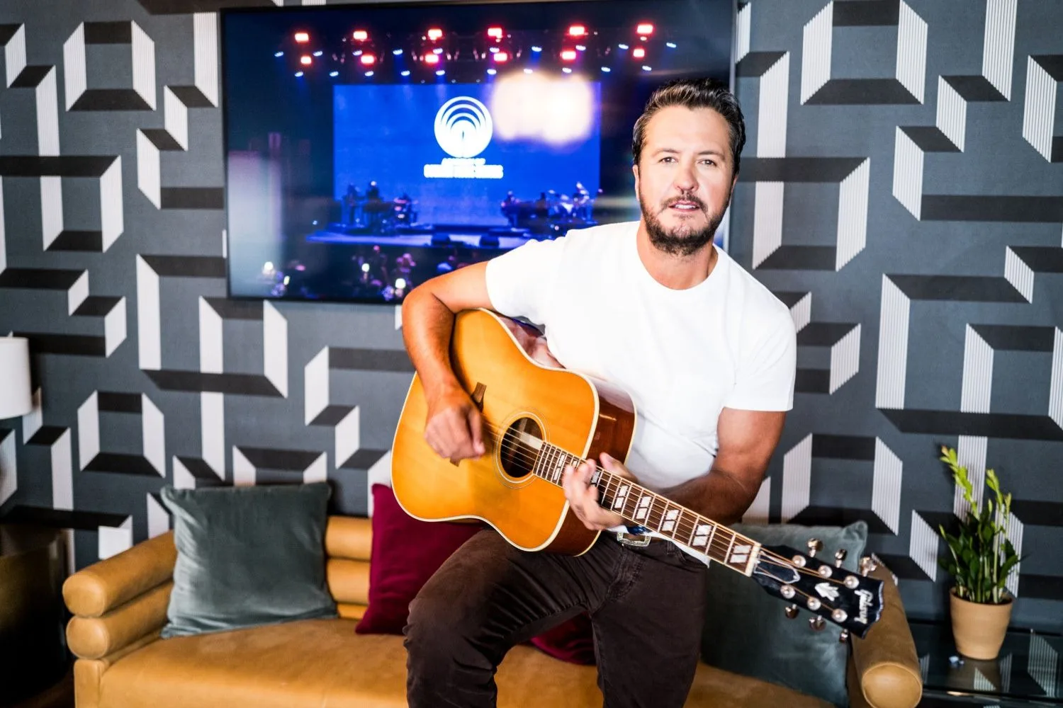 luke bryan on a stool with a guitar smiling for the camera