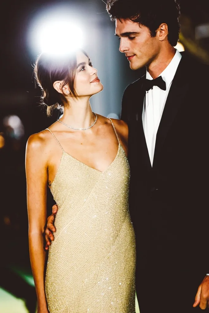 Kaia Gerber and Jacob Elordi on the red carpet smiling at each other.