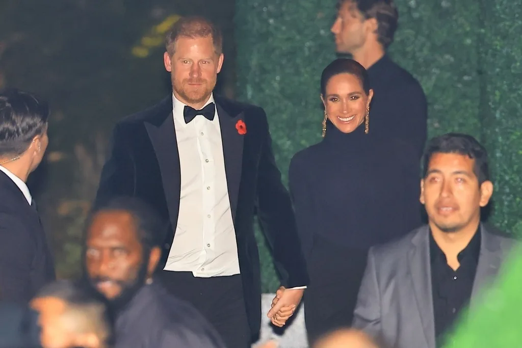 prince harry in a tux, holding hands with meghan markle who is smiling in a black dress