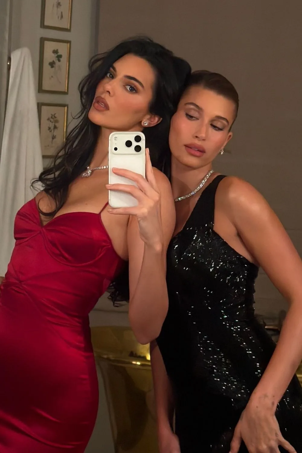 Kendall Jenner in a red dress leaning on Hailey Bieber for a mirror selfie