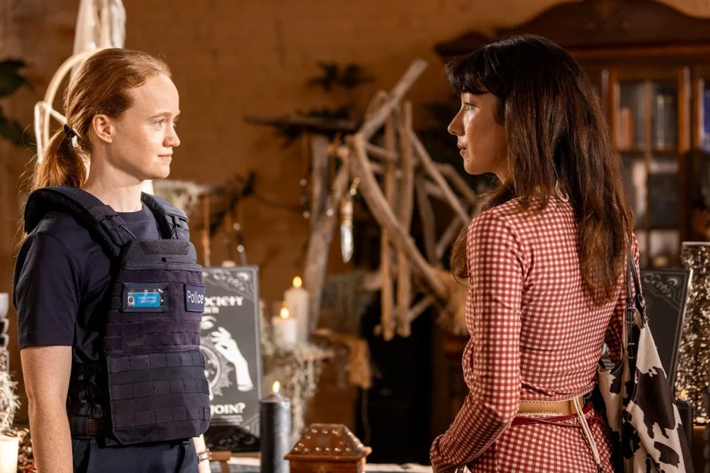 liv hewson on the left in a cop uniform and natasha on the right dressed in a red and white gingham outfit, having a tense conversation