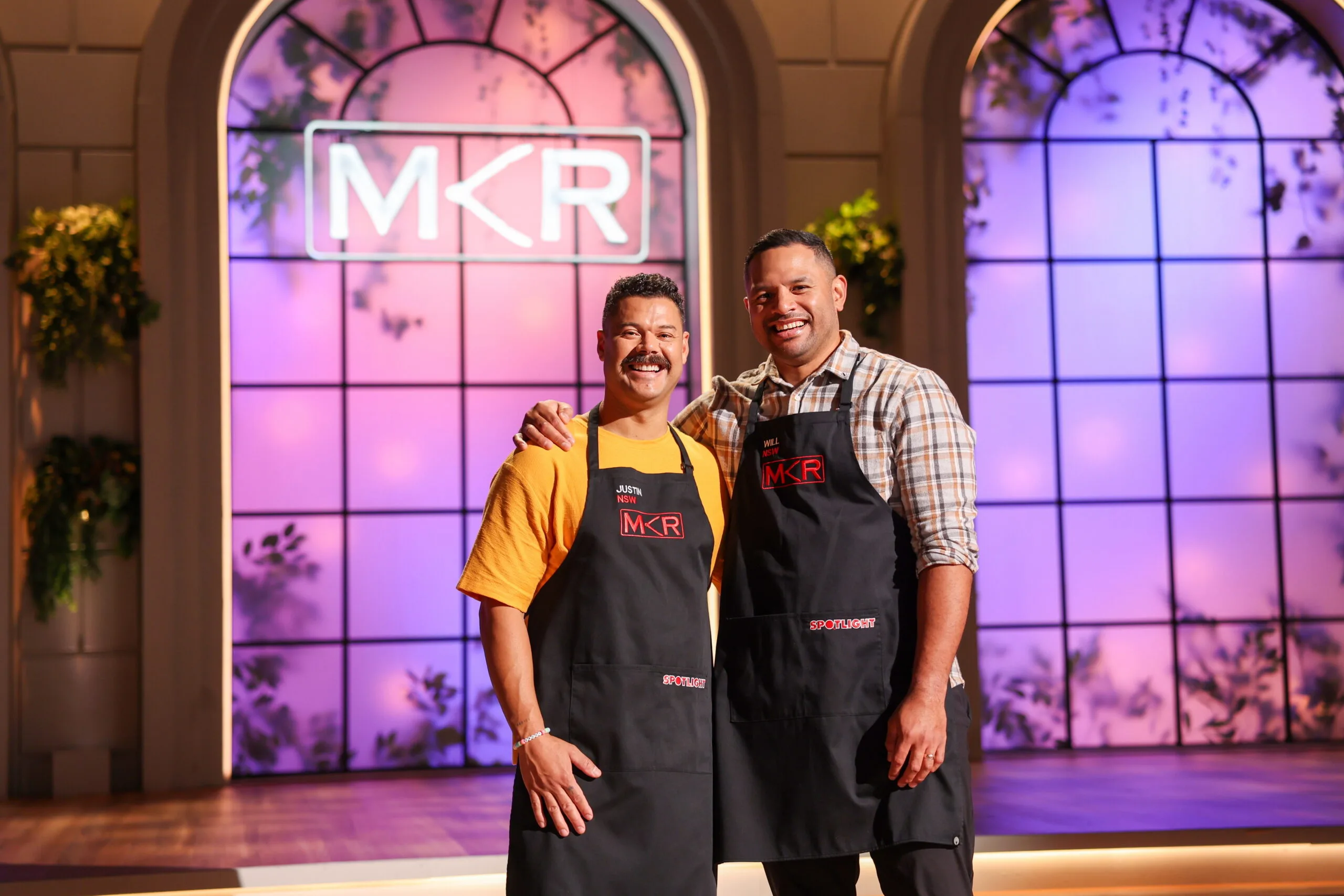 two men posing together in aprons in front of large wondows
