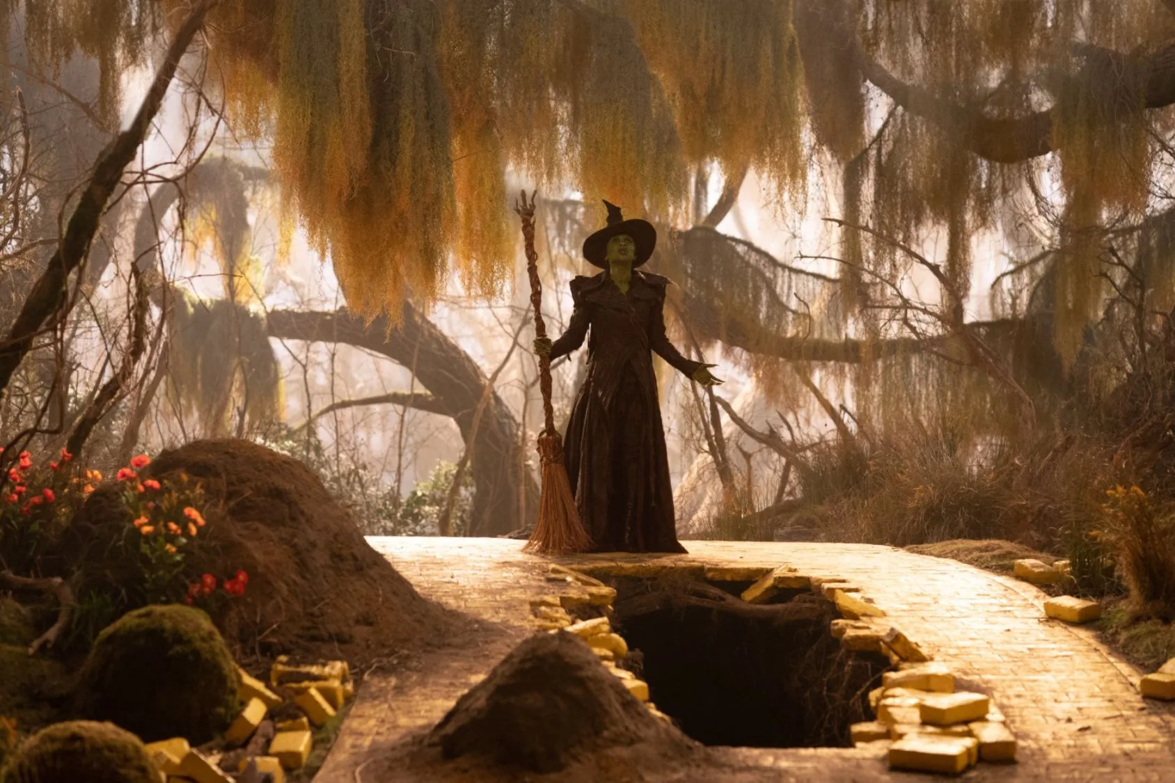 elphaba in her treehouse dressed in black clothing and a pointy hat holding a broomstick