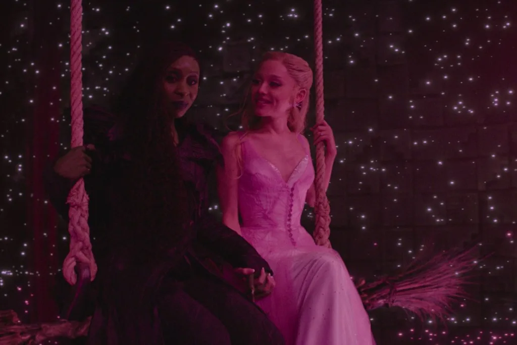 elphaba and glinda sitting on the broomstick in a darkly lit room with hot pink lighting