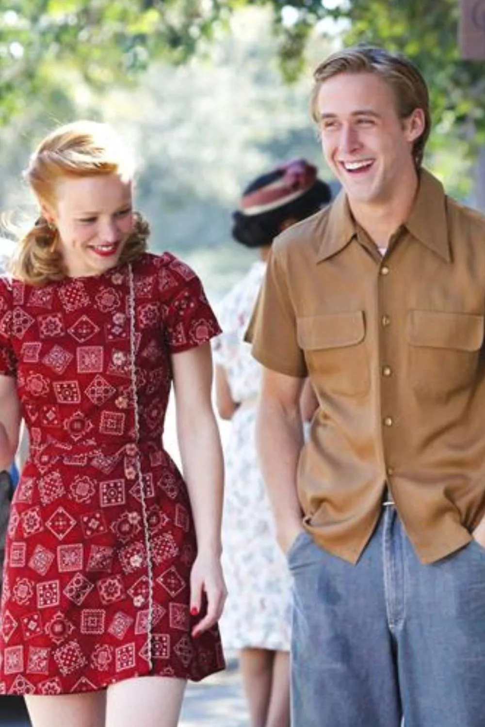 The Notebook: Woman with orange hair in a red mini dress walking next to a man in a tan shirt and shorts smiling.