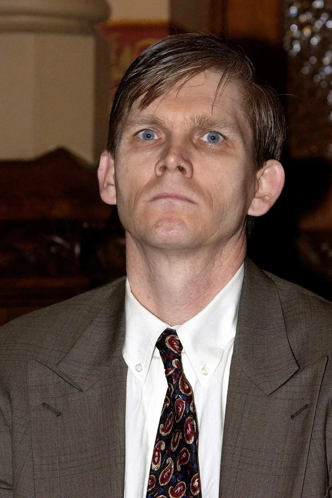 ted maher, a gaunt pale man looking serious at the camera in a suit