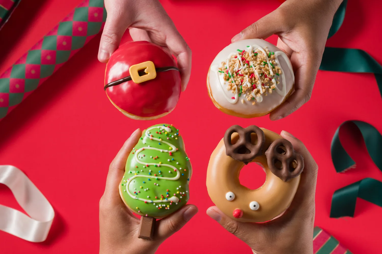 Four Krispy Kreme Christmas doughnuts being held. 