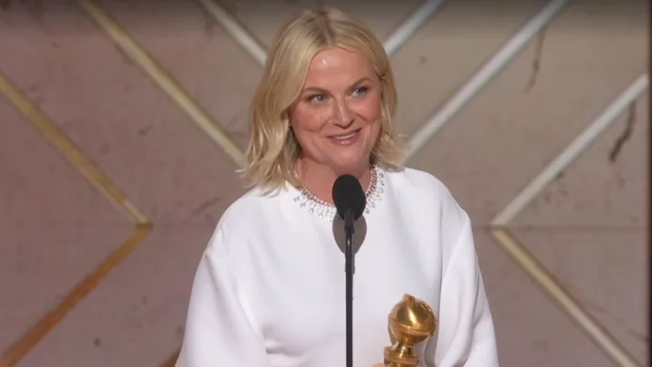 Amy Poehler accepts her Golden Globe for best podcast wearing a white dress.