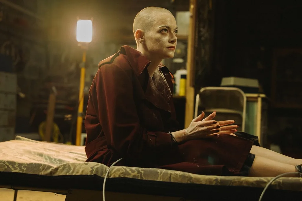 emma stone bald in a dimly lit basement