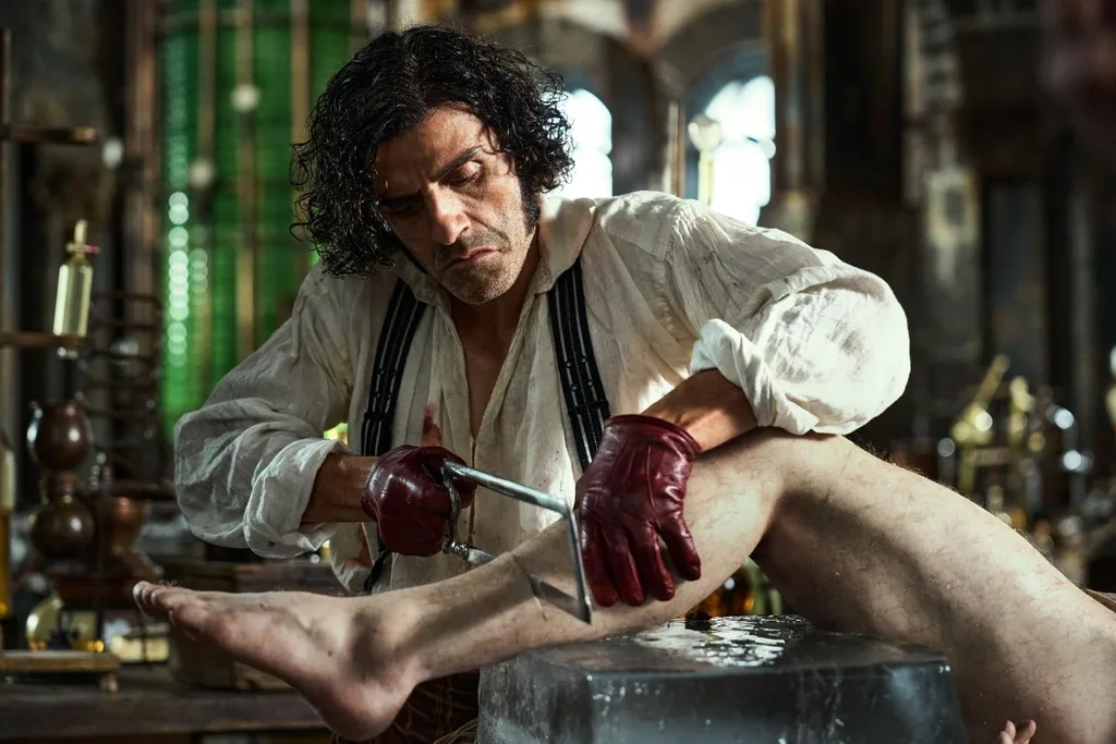 oscar isaac in character as dr frankenstein sawing off a leg