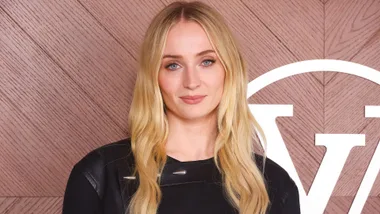 Sophie Turner smiling in front of pink media wall.