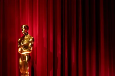 a gold oscars 2026 award in front of a red curtain