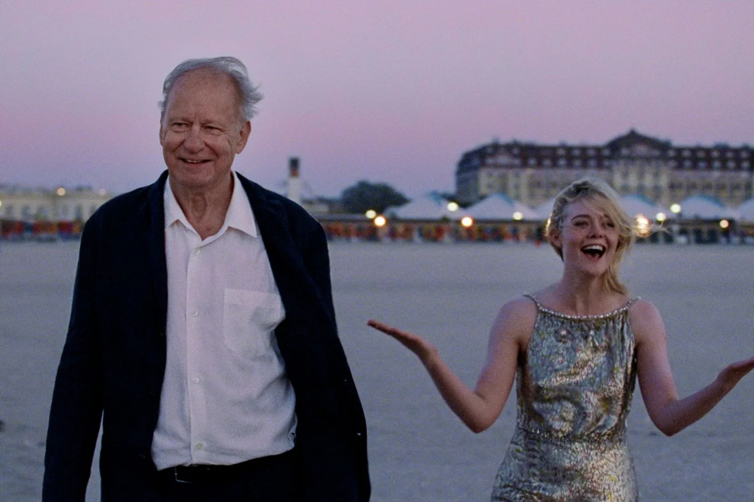 an older man and a young woman smiling on a beach at dusk
