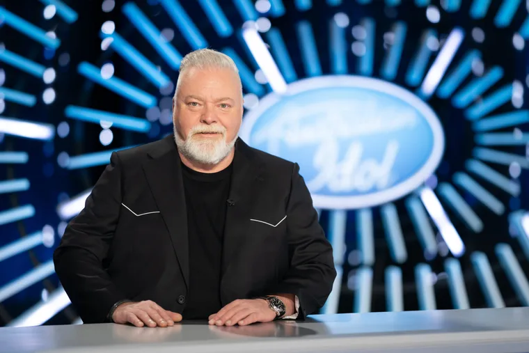 kyle sandilands in a balck suit posing at the australian idol judges table