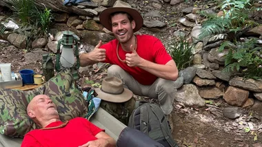 Barry Williams lies asleep in a camp bed with Matt doing a 'thumbs up' gesture.