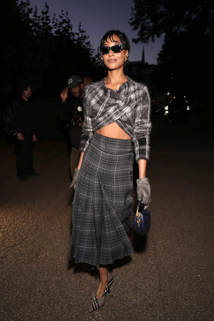 Woman wearing a check top and skirt posing with sunglasses on.