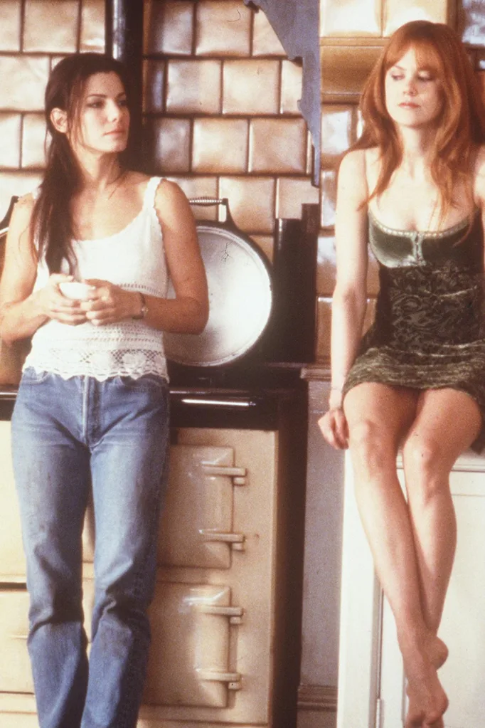 Witchcraft: Woman standing in white tank top and jeans looking at a woman in a green dress for the movie Pratical Magic.