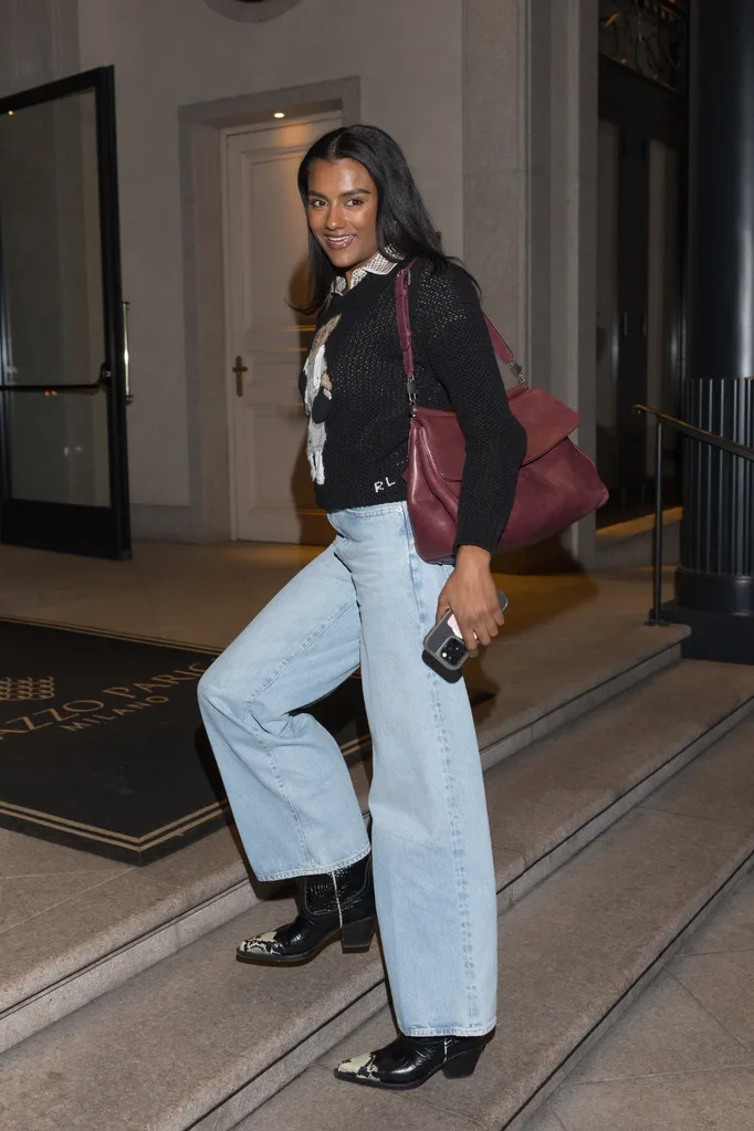 Woman posing as shes walking up stairs wearing a printed jumper and blue jeans with boots.
