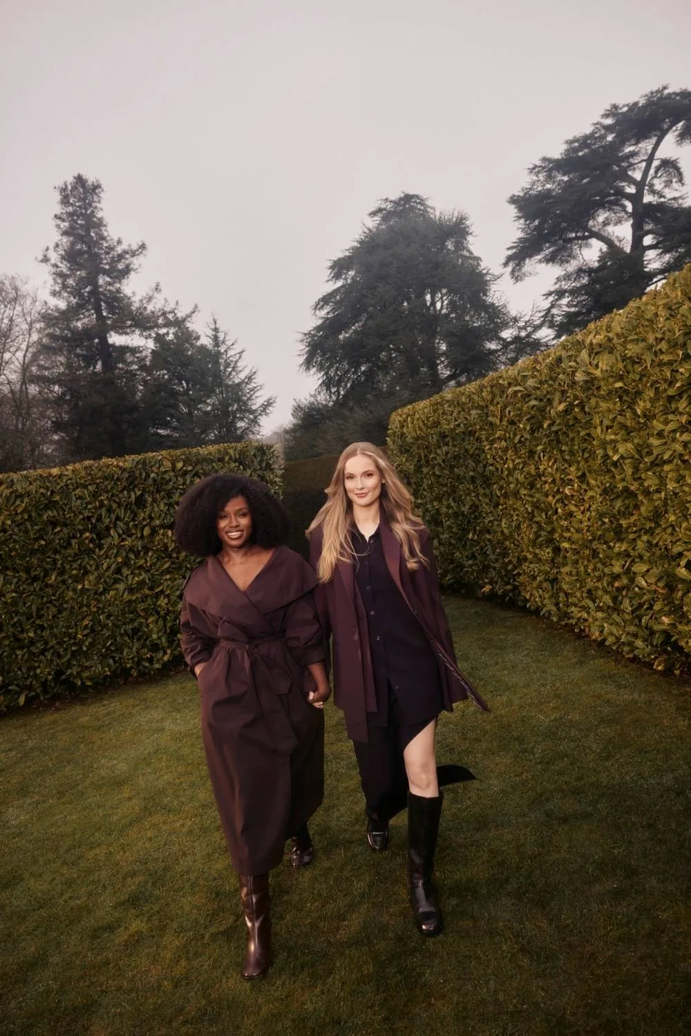 two women walk hand in hand through a garden