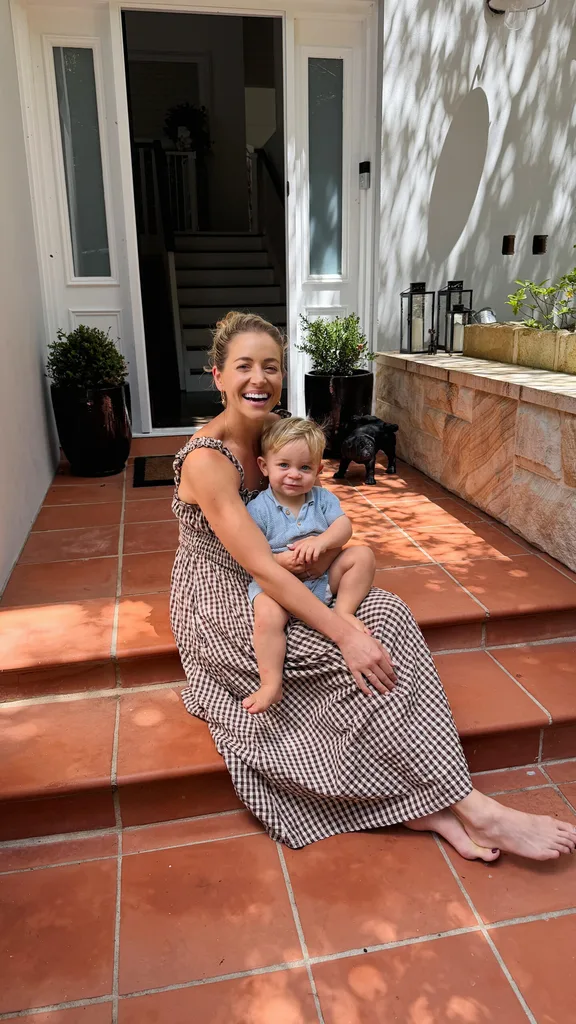holly kingston smiling widely while her young son lennox sits in her lap on the stairs of their home