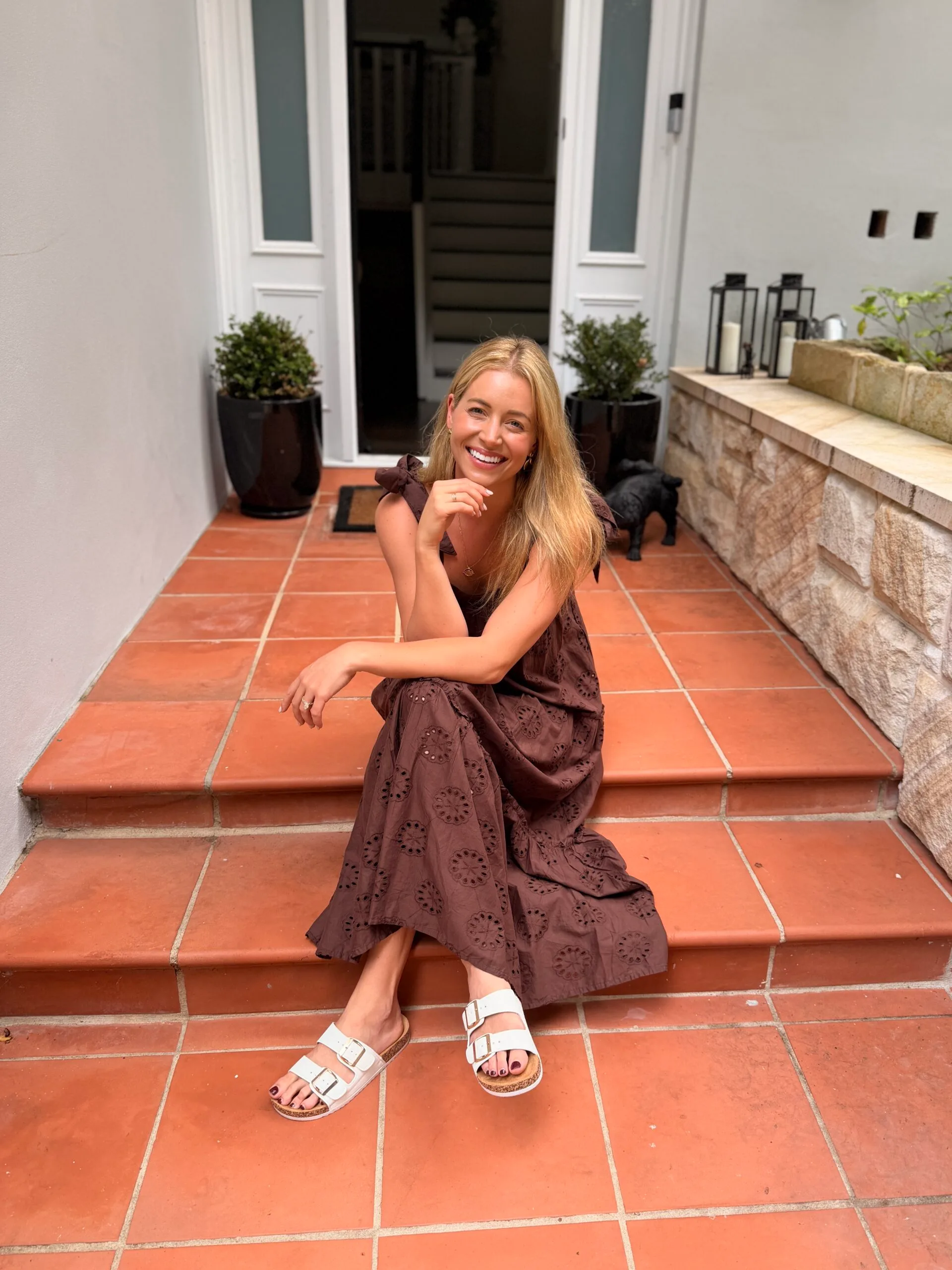 holly kingston sits on the steps of her house while smiling into the camera