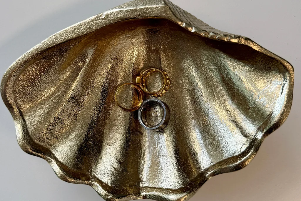A silver Oura ring in a jewellery dish surrounded by other gold rings.