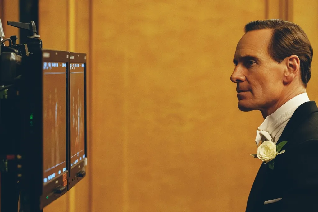 michael fassbender in character on set of Kennedy looking at the camera screens against a yellow backdrop