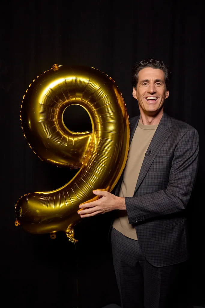 andy lee smiling while holding a gold '9' balloon