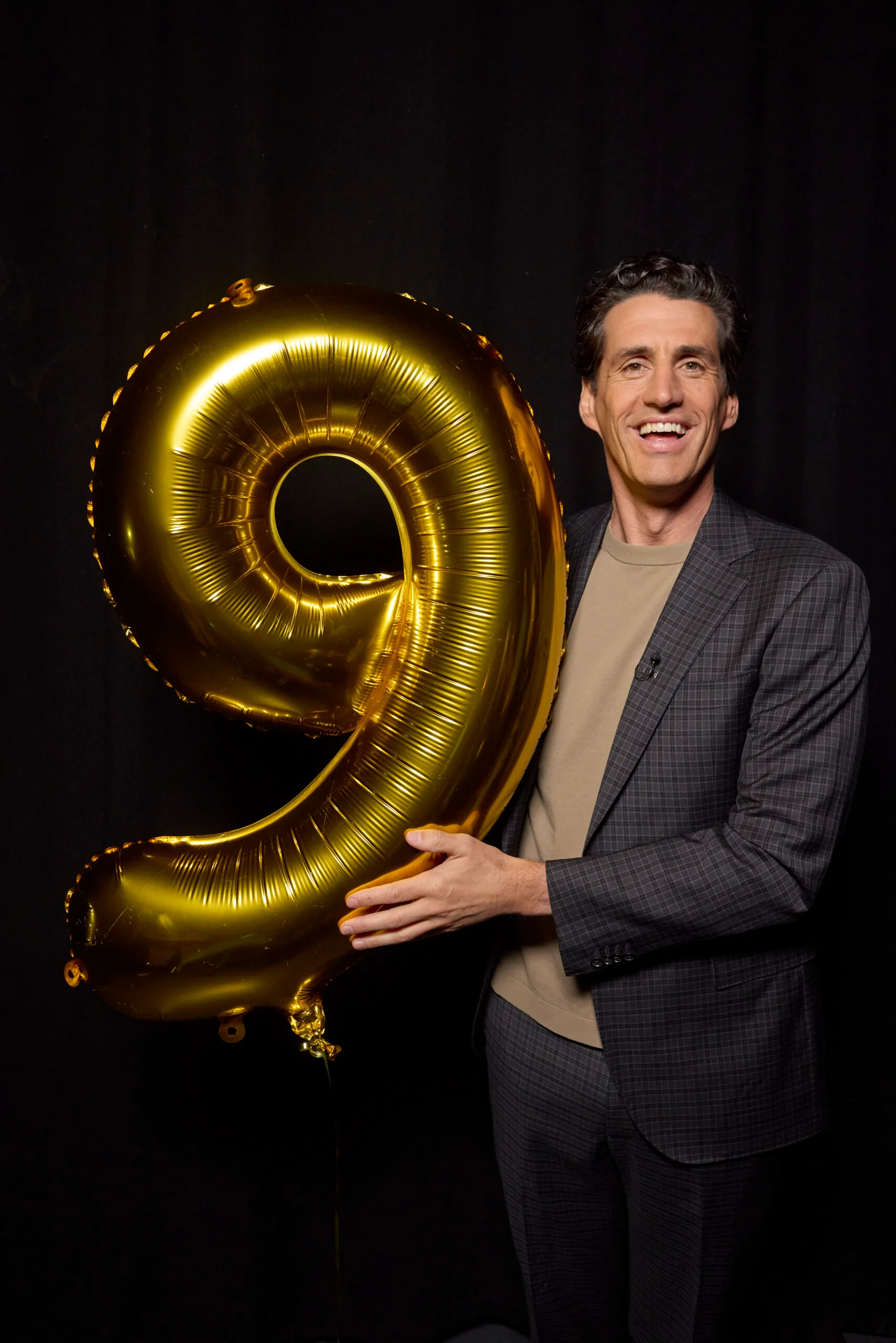 andy lee smiling while holding a gold '9' balloon