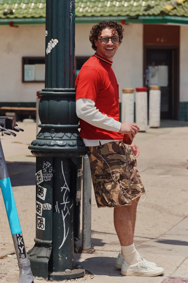 Belmon Cameli fearing a red and white longslever and cargo shorts with white reeboks.