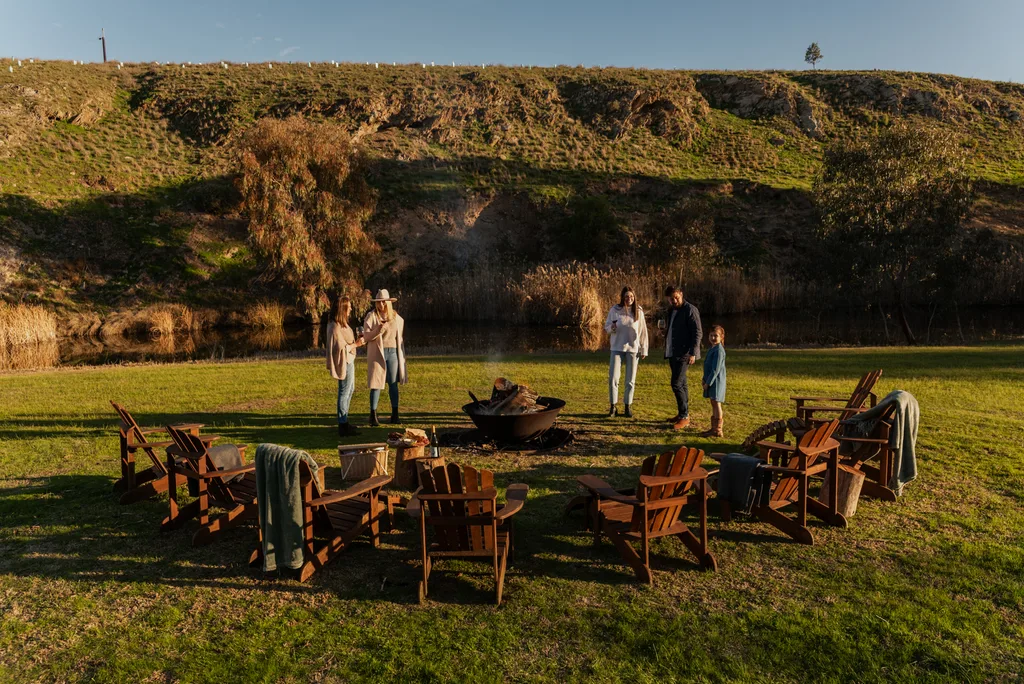 People mill about a firepit against rolling green hills.