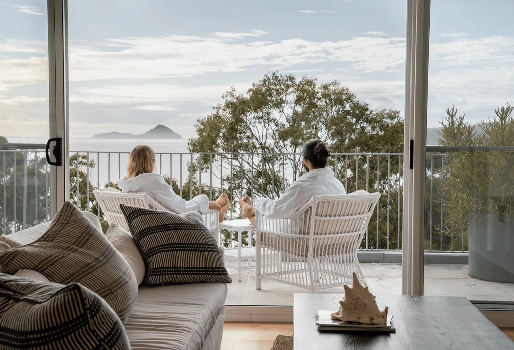A couple in white robes sit on a balcony looking out at the sea.
