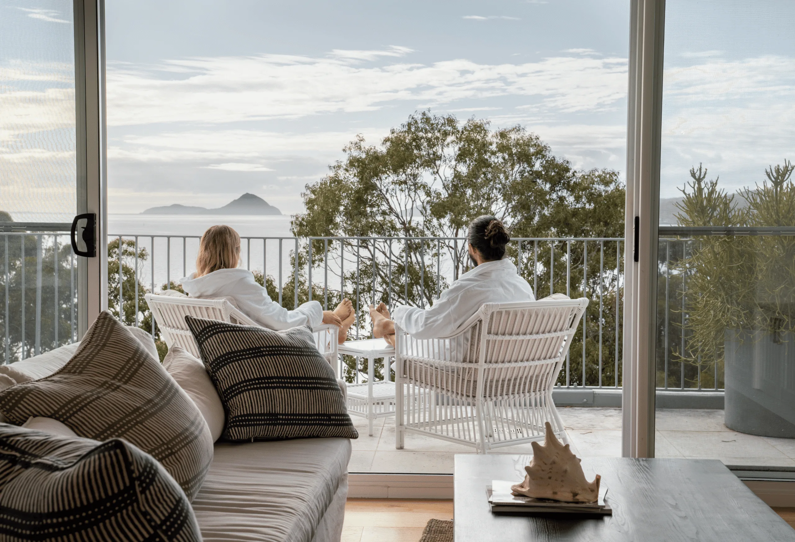 A couple in white robes sit on a balcony looking out at the sea. 