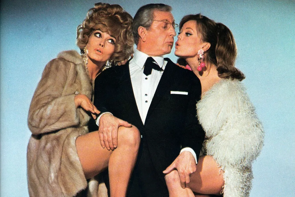 A threesome of one man (middle) and two women (left and right) wearing fur coats.