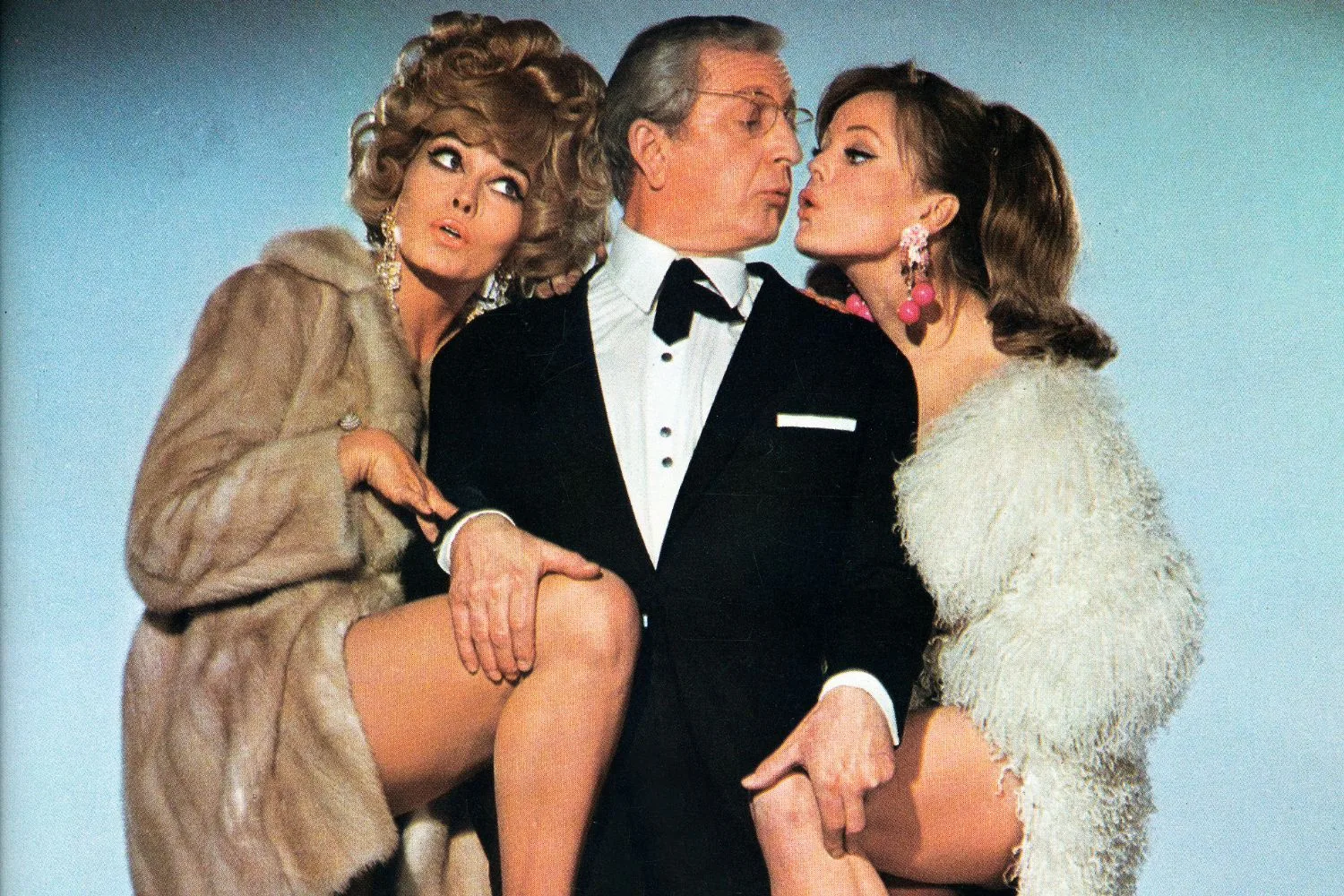 A threesome of one man (middle) and two women (left and right) wearing fur coats.